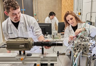 Three researchers wearing white lab coats, working with machinery and digital screens in the 91㽶Ƶ Advanced Engineering Centre